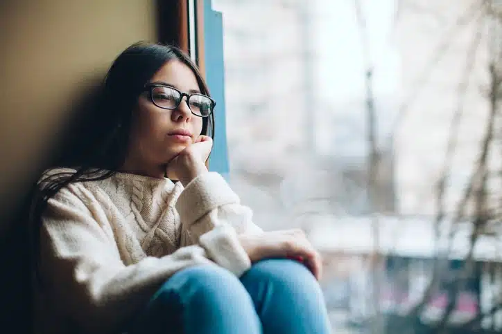 A teenage girl struggling with depression sits by a window